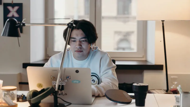 Fokussierter junger Mann arbeitet an seinem Schreibtisch mit einem Laptop in einem modernen Büro.