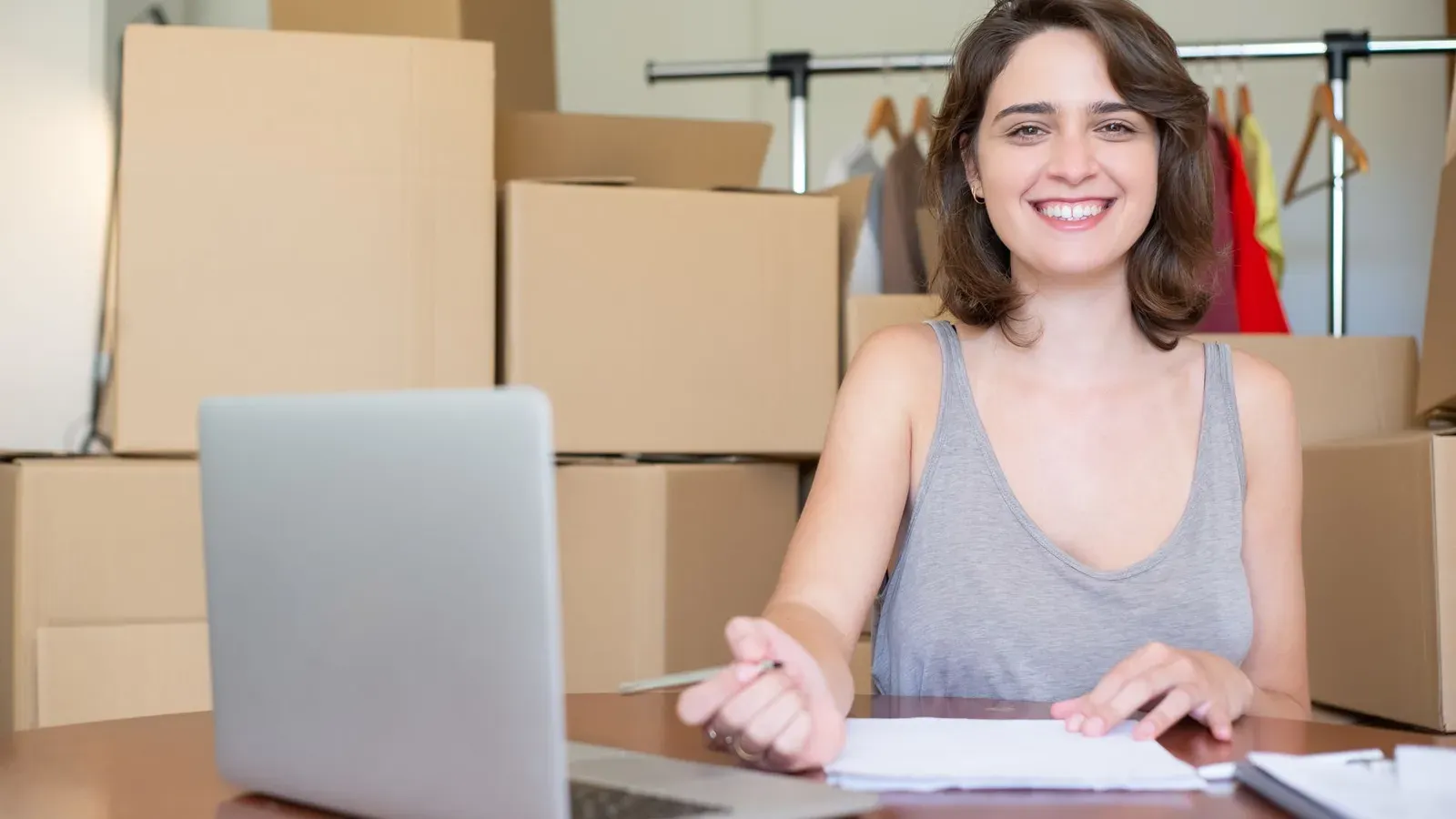 Glückliche Frau, die an einem Laptop arbeitet, umgeben von Kartons. Ideal für Geschäfts- und Online-Shop-Konzepte.