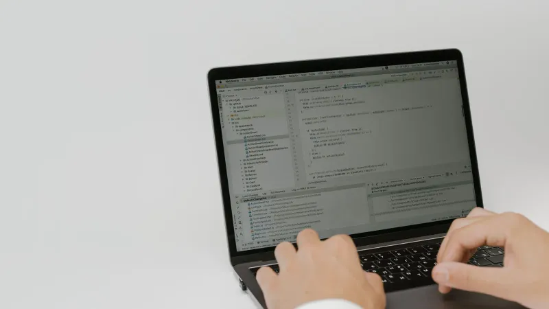 Hände tippen Code auf einem Laptop in einem Arbeitsplatz. Innere Umgebung, die sich auf Softwareentwicklung konzentriert.