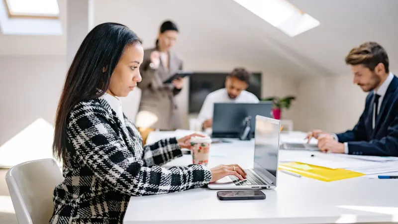 Geschäftsfachleute arbeiten in einer modernen, kollaborativen Büroumgebung mit Laptops.