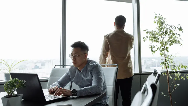 Zwei Männer arbeiten in einem modernen Büro mit großen Fenstern und Blick auf die Stadt.