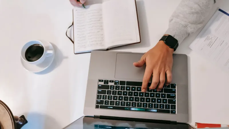 Eine Blick von oben auf ein Home-Office-Setup mit einem Laptop, Notizbuch und Kaffee.