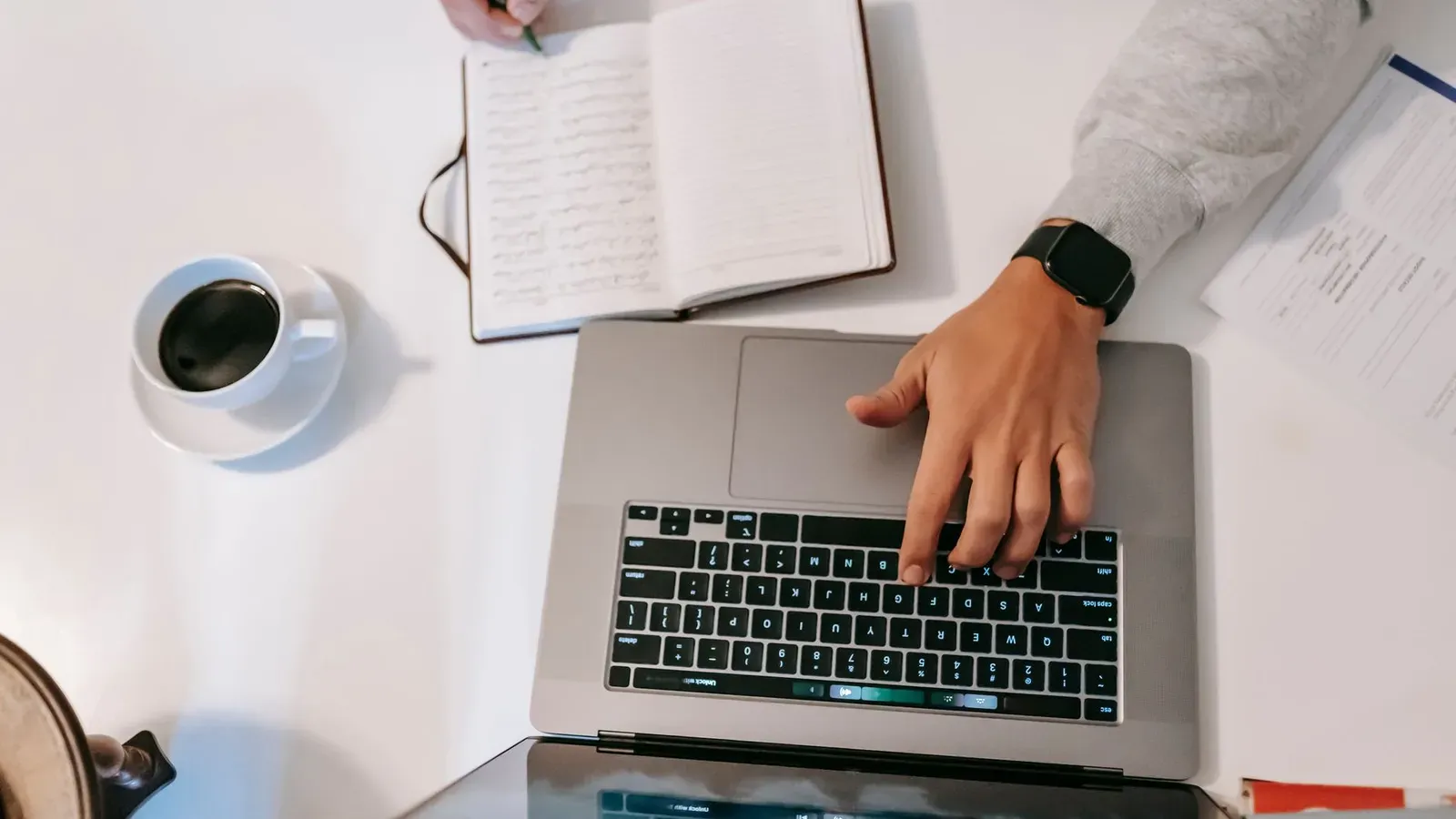 Eine Blick von oben auf ein Home-Office-Setup mit einem Laptop, Notizbuch und Kaffee.