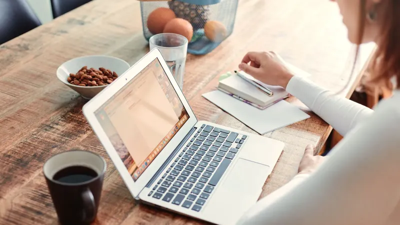 Frau arbeitet zu Hause mit einem Laptop, Kaffee und gesunden Snacks auf einem Holztisch.