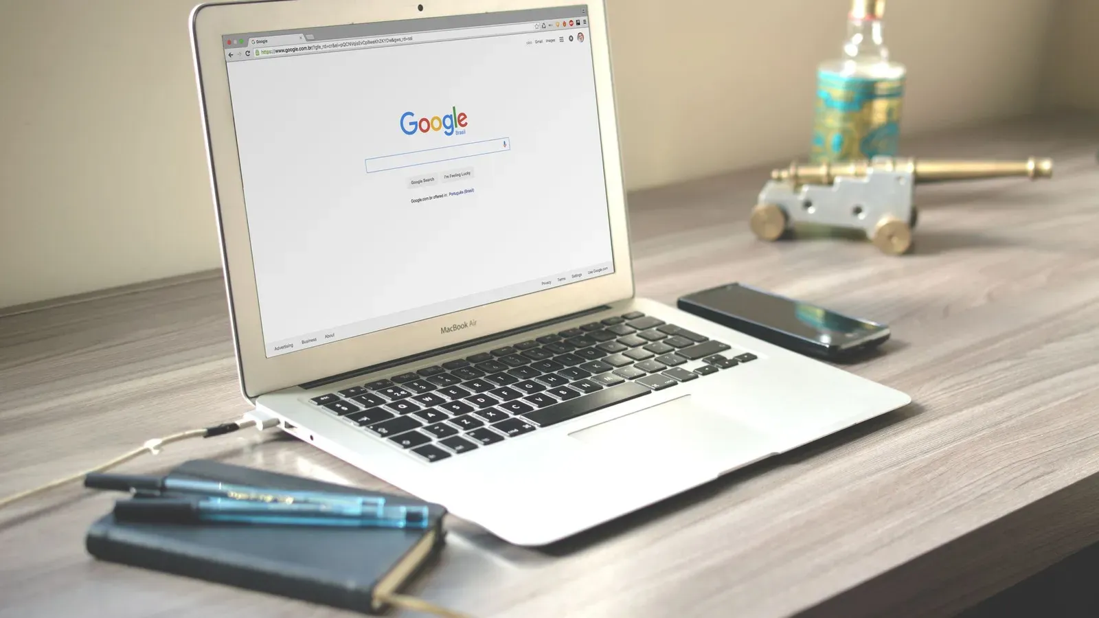 Ein ordentlicher Arbeitsplatz mit einem Laptop, der die Google-Suche anzeigt, einem Smartphone und einem Notizbuch auf einem Holztisch.